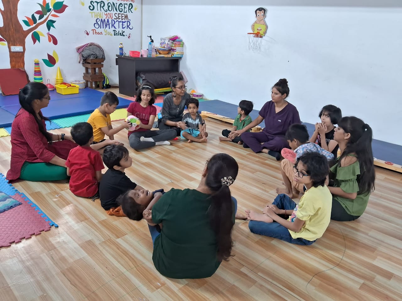 A therapist leads a circle-time session with a group of children on the therapy floor.