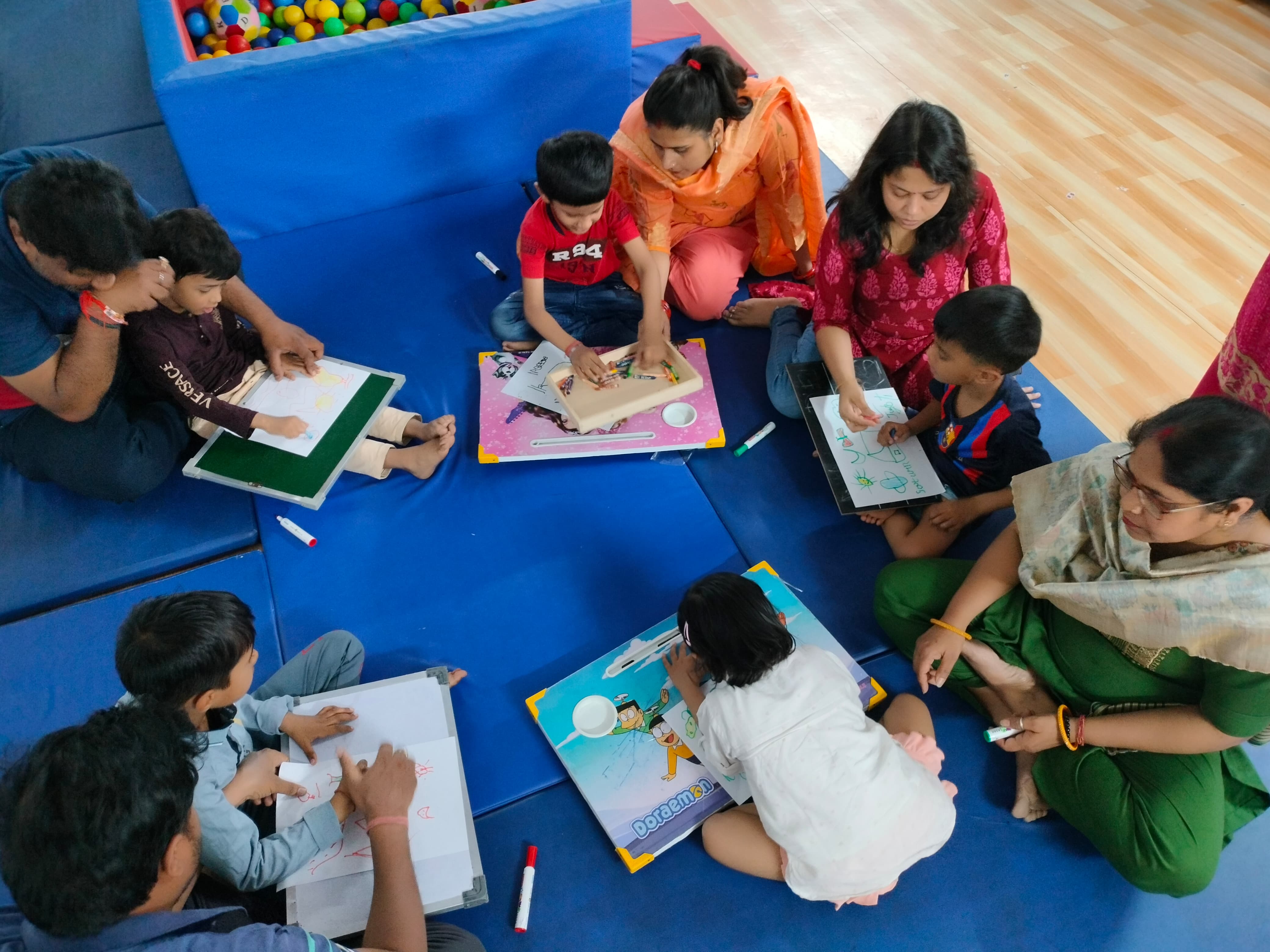 An overhead view of children drawing on lap boards during an occupational therapy activity, supported by therapists and parents.